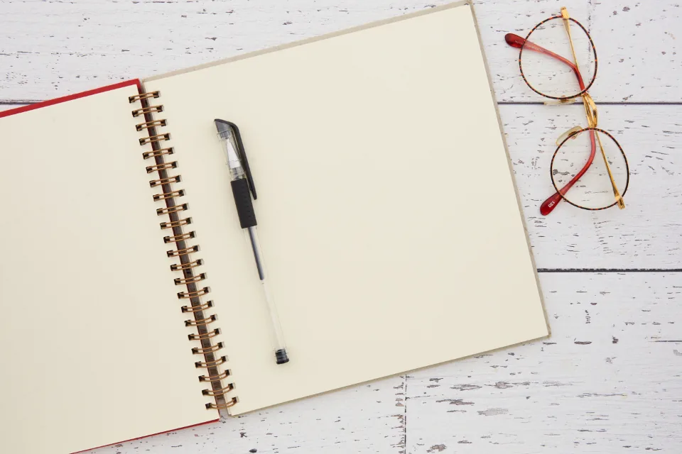 Beyaz ahşap masada açık defter, kalem ve gözlük